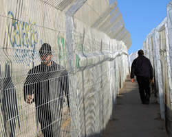 PALESTINIANS WALK IN FENCED LANES BESIDE ISRAELI SECURITY FENCE – Palestinians walk in fenced lanes beside the 30-foot-high Israeli security wall at the entrance to Bethlehem in the West Bank Dec. 19. The wall has created hardship for Palestinians, who must obtain a special permit to cross the Israeli-controlled check point into Jerusalem. Israel maintains that the wall is needed to ensure its security. (CNS)